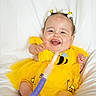 Raelynn is registered to the contest to win money with this photo: baby, child, yellow_dress, bee_theme, hair_accessories, smiling, happy, infant, medical_tube, cute, sitting, white_background, plush, toddler, portrait, clothing, face, person, indoors, bright