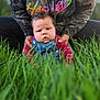 Michael is registered to the contest to win money with this photo: baby, child, denim_overalls, red_shirt, adult_hands, hoodie, grass, outdoor, portrait, serious_expression, person, nature, greenery, casual_clothing, closeup, face, sitting, daylight, young_child, holding