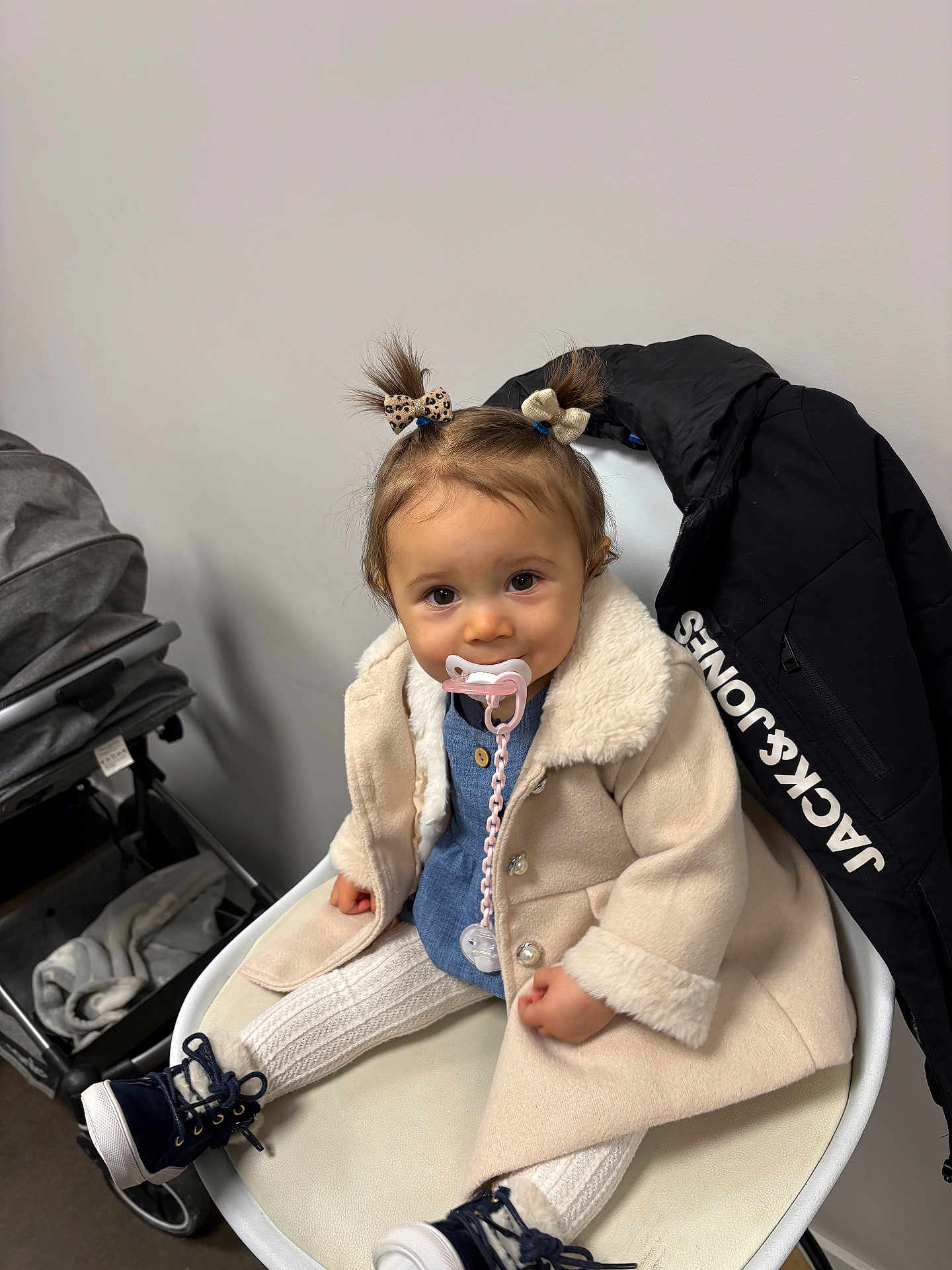Tahyssia participe au concours pour gagner de l'argent avec cette photo : toddler, child, pacifier, coat, pigtails, bow, chair, jacket, stroller, white_wall, boots, knitted_leggings, indoor, cute, sitting, clothing, baby, person, accessory, smiling