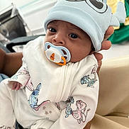 Kioshy participe au concours pour gagner de l'argent avec cette photo : baby, infant, pacifier, hat, onesie, cartoon_print, hand, closeup, portrait, cute, indoor, child, person, soft_lighting, expression, white_clothing, cartoon_characters, newborn, holding, face