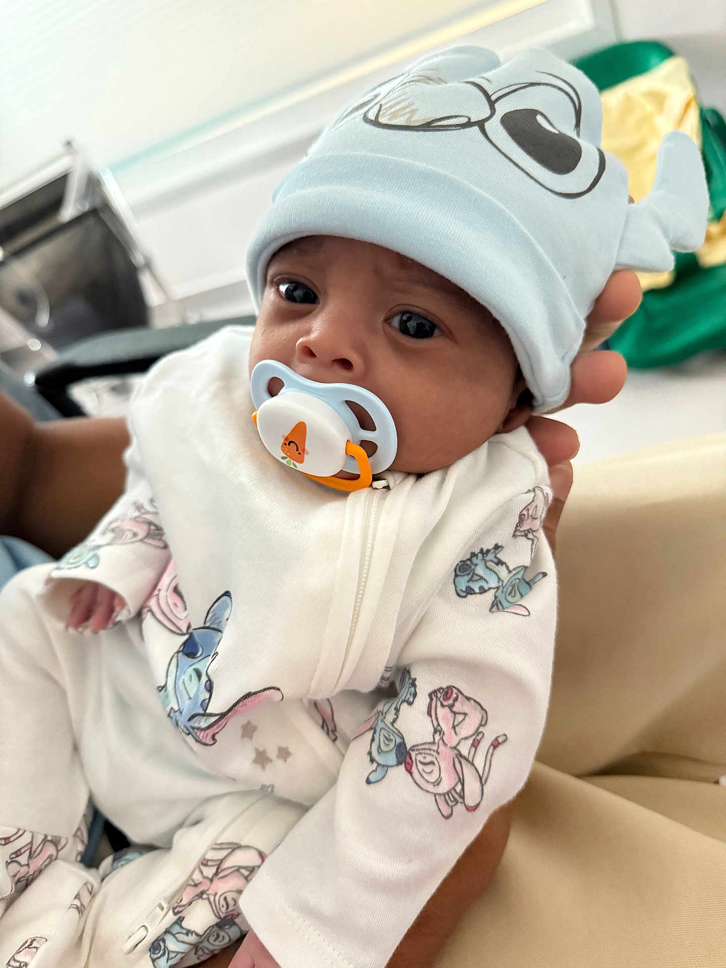Kioshy participe au concours pour gagner de l'argent avec cette photo : baby, infant, pacifier, hat, onesie, cartoon_print, hand, closeup, portrait, cute, indoor, child, person, soft_lighting, expression, white_clothing, cartoon_characters, newborn, holding, face
