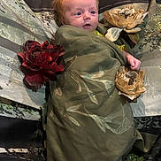 Aurora is registered to the contest to win money with this photo: baby, child, green_cloth, flower, artificial_flower, wrapped, portrait, face, red_hair, nature_theme, background, indoor, cute, lying_down, decor, soft_lighting, expression, infant, small_hands, cozy
