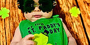 Emanuel joined the competition — help win amazing prizes! baby, background_decoration, bib, child, closeup, clover, cute, diaper, face, green_clothing, holiday, infant, lying_down, playful, portrait, props, shamrock, st_paddys_day, sunglasses, wooden_floor