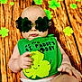 baby, background_decoration, bib, child, closeup, clover, cute, diaper, face, green_clothing, holiday, infant, lying_down, playful, portrait, props, shamrock, st_paddys_day, sunglasses, wooden_floor