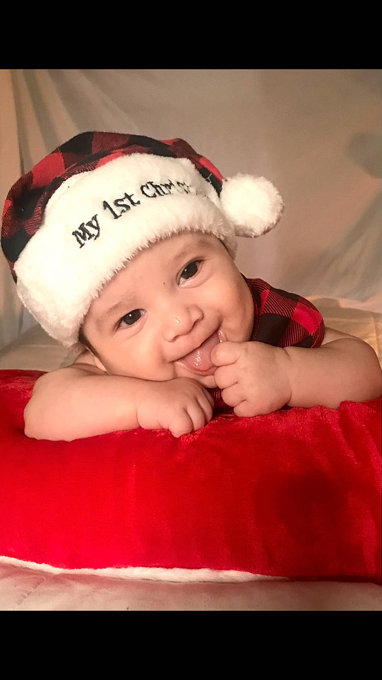 Israel is registered to the contest to win money with this photo: baby, baby_toddler_clothing, cap, cheek, child, christmas, christmas_eve, comfort, fictional_character, flash_photography, fun, happy, headwear, holiday, knit_cap, magenta, person, pink, rectangle, sleeve