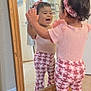 toddler, child, mirror, reflection, pink_clothing, headband, happy, smiling, indoor, tile_floor, wooden_frame, pants, short_sleeves, baby, home, person, cute, playful, expression, standing