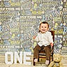 toddler, child, birthday, celebration, chair, teddy_bear, smiling, one_year_old, white_shirt, brown_pants, floor, sign, happy, indoors, portrait, festive, decorations, chalkboard, colorful, wooden_chair