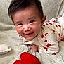 baby, smiling, heart_pattern, onesie, blanket, plush_heart, toddler, cute, happy, portrait, indoor, soft_texture, infant, child, face, lying_down, cozy, red, white, hands