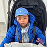 baby_boy, blanket, blue_cap, blue_jacket, child, cute, door, expression, hand, harness, hat, indoor, portrait, pram, puffy_jacket, seatbelt, stroller, tiled_floor, toddler, winter_clothing