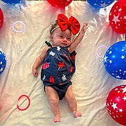 Raelynn is registered to the contest to win money with this photo: baby, infant, bow, headband, balloons, red_balloons, blue_balloons, stars, blanket, carpet, laying_down, one_arm_raised, cute, child, indoors, celebration, patterned_clothing, colorful, soft_texture, smiling