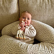 Marceau a rejoint le concours — aidez-le/la à gagner de superbes lots ! baby, infant, teething_toy, giraffe_toy, pillow, polka_dot, couch, beige, cozy, child, cute, indoors, soft_lighting, sweater, hand, face, person, comfort, seated, curious
