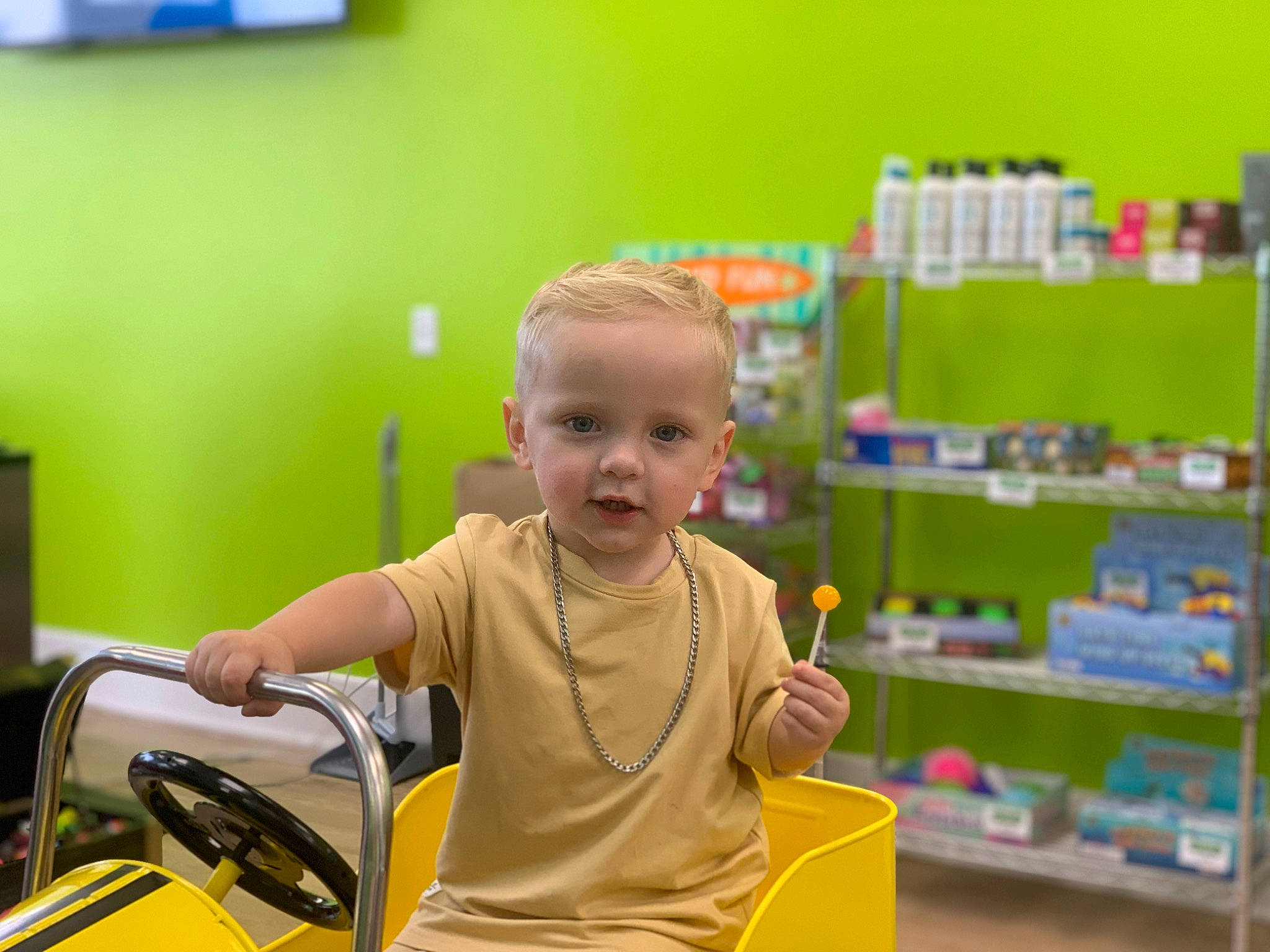 Tylin is registered to the contest to win money with this photo: baby, building, child, customer, fun, happy, leisure, motor_vehicle, person, retail, riding_toy, room, service, shelf, shelving, smile, t_shirt, toddler, toy, toy_vehicle