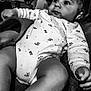 Djamaïly a rejoint le concours — aidez-le/la à gagner de superbes lots ! baby, black_and_white, blanket, child, closeup, clothing, cozy, curious, cute, expression, face, hand, indoor, infant, leg, lying_down, onesie, portrait, soft, young