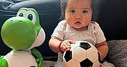 Giselle is registered to the contest to win money with this photo: baby, child, toy, dinosaur_toy, soccer_ball, blanket, couch, indoor, cute, portrait, infant, soft_lighting, playtime, casual_clothing, person, seated, expression, hair_tie, red_bracelet, floor
