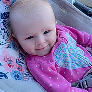 Natalie is registered to the contest to win money with this photo: baby, infant, smile, pink_clothing, polka_dot, floral_pattern, baby_seat, car_seat, child, cute, happy, indoors, face, person, young_child, blue_eyes, soft_toys, comfort, seatbelt, hair