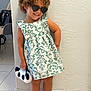 child, girl, curly_hair, dress, sunglasses, purse, panda, white_bow, smile, standing, indoor, tile_floor, bracelet, wall, footwear, sandals, cute, fashion, accessories, happy