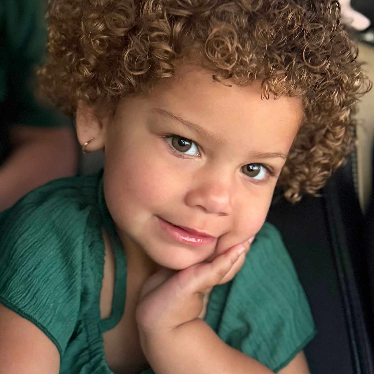 Allisson joined the competition — help win amazing prizes! apparel, child, closeup, curly_hair, cute, earring, expression, eyes, face, green_clothing, hair, hand, indoors, person, portrait, resting, skin, smile, toddler, young_child