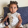 toddler, child, baby, curly_hair, pigtails, white_onesie, bunny_embroidered, blanket, pillow, patterned_pillow, indoor, sitting, cute, portrait, face, hand, toy, pacifier_clip, soft_lighting, wall
