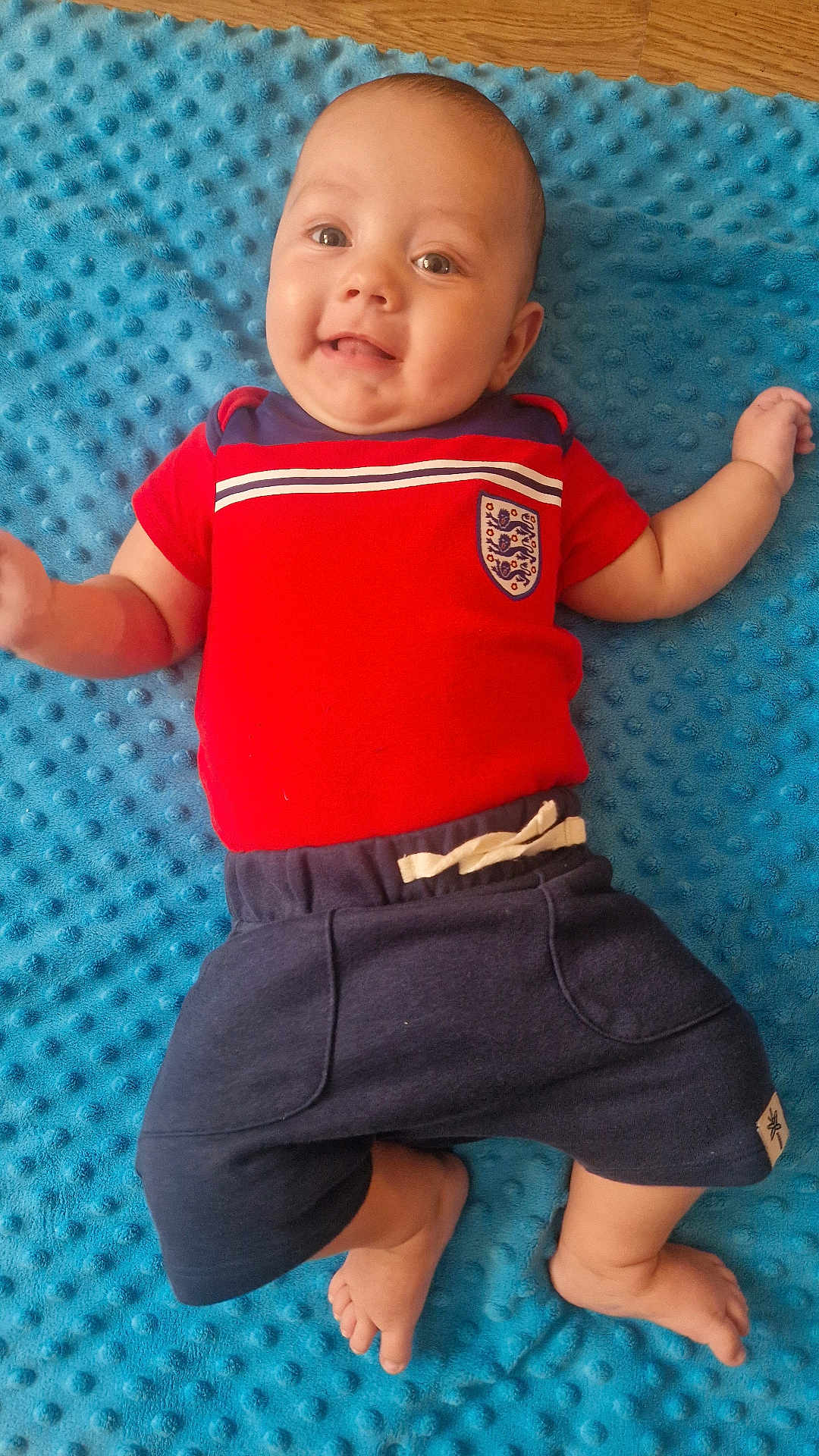 Carter-Ross joined the competition — help win amazing prizes! baby, child, smile, red_shirt, navy_shorts, blue_blanket, infant, cute, happy, lying_down, barefoot, portrait, indoors, person, small_child, soft_texture, casual_clothing, young, playful, comfortable