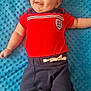 baby, child, smiling, red_shirt, blue_pants, blanket, floor, happy, infant, cute, one_person, indoors, skin, foot, head, face, clothing, lying_down, casual, portrait