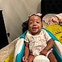 baby, infant, smiling, pink_bows, baby_seat, bedroom, bed, blanket, yellow_blanket, pink_blanket, headboard, smile, happy, child, person, indoor, clothing, white_shirt, light_pink_dress, cute