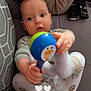 Nolan participe au concours pour gagner de l'argent avec cette photo : baby, child, toy, maraca, hand, face, curious, pillow, couch, clothing, socks, person, indoor, comfort, cute, infant, holding, patterned_pants, warm, relaxed