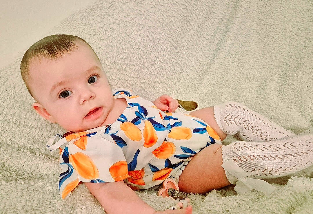 Maïna a rejoint le concours — aidez-le/la à gagner de superbes lots ! baby, baby_toddler_clothing, child, collar, comfort, flooring, foot, grass, happy, human_leg, pattern, person, portrait_photography, sitting, sleeve, toddler, wood