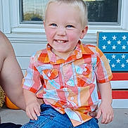 Cameron is registered to the contest to win money with this photo: child, toddler, smiling, plaid_shirt, denim_shorts, blue_eyes, sitting, person, outdoor, porch, window, decoration, stars, stripes, happy, cute, face, short_hair, summer, casual_clothing