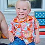 child, toddler, smiling, plaid_shirt, denim_shorts, blue_eyes, sitting, person, outdoor, porch, window, decoration, stars, stripes, happy, cute, face, short_hair, summer, casual_clothing