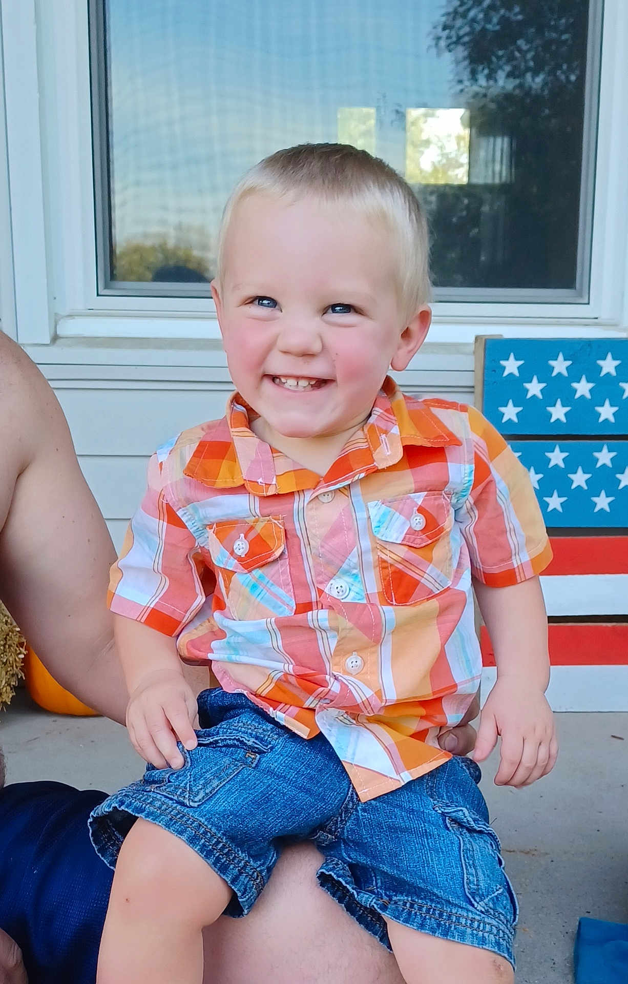 Cameron is registered to the contest to win money with this photo: child, toddler, smiling, plaid_shirt, denim_shorts, blue_eyes, sitting, person, outdoor, porch, window, decoration, stars, stripes, happy, cute, face, short_hair, summer, casual_clothing