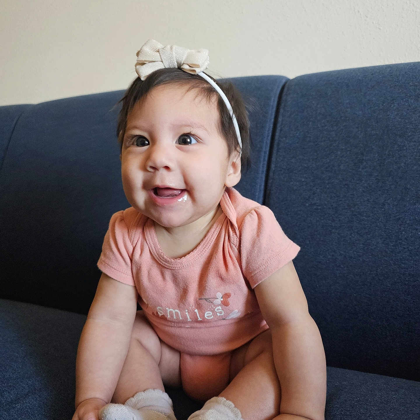 Aithana is registered to the contest to win money with this photo: baby, child, infant, smiling, sitting, couch, headband, onesie, peach, happy, cute, indoor, portrait, sock, hand, face, young, person, expression, furniture