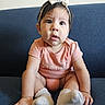 baby, infant, child, onesie, headband, bow, socks, couch, blue_couch, curious, wide_eyes, sitting, indoor, portrait, person, cute, expression, clothing, skin, smile