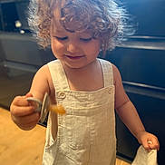 Achille a rejoint le concours — aidez-le/la à gagner de superbes lots ! toddler, child, curly_hair, overalls, indoor, spoon, food, cloth, smile, happy, person, baby, light, wooden_floor, cabinet, play, cute, small, standing, apparel