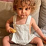 Achille a rejoint le concours — aidez-le/la à gagner de superbes lots ! toddler, child, curly_hair, overalls, bread, snack, couch, beige, indoor, person, sitting, cute, young_child, clothing, furniture, expression, food, casual, portrait, home