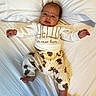 baby, infant, child, portrait, lying_down, bed, pillow, white_bedding, sweater, pajamas, teddy_bears, clothing, face, eyes, smiling, arms_outstretched, bare_feet, indoor, cozy, photography