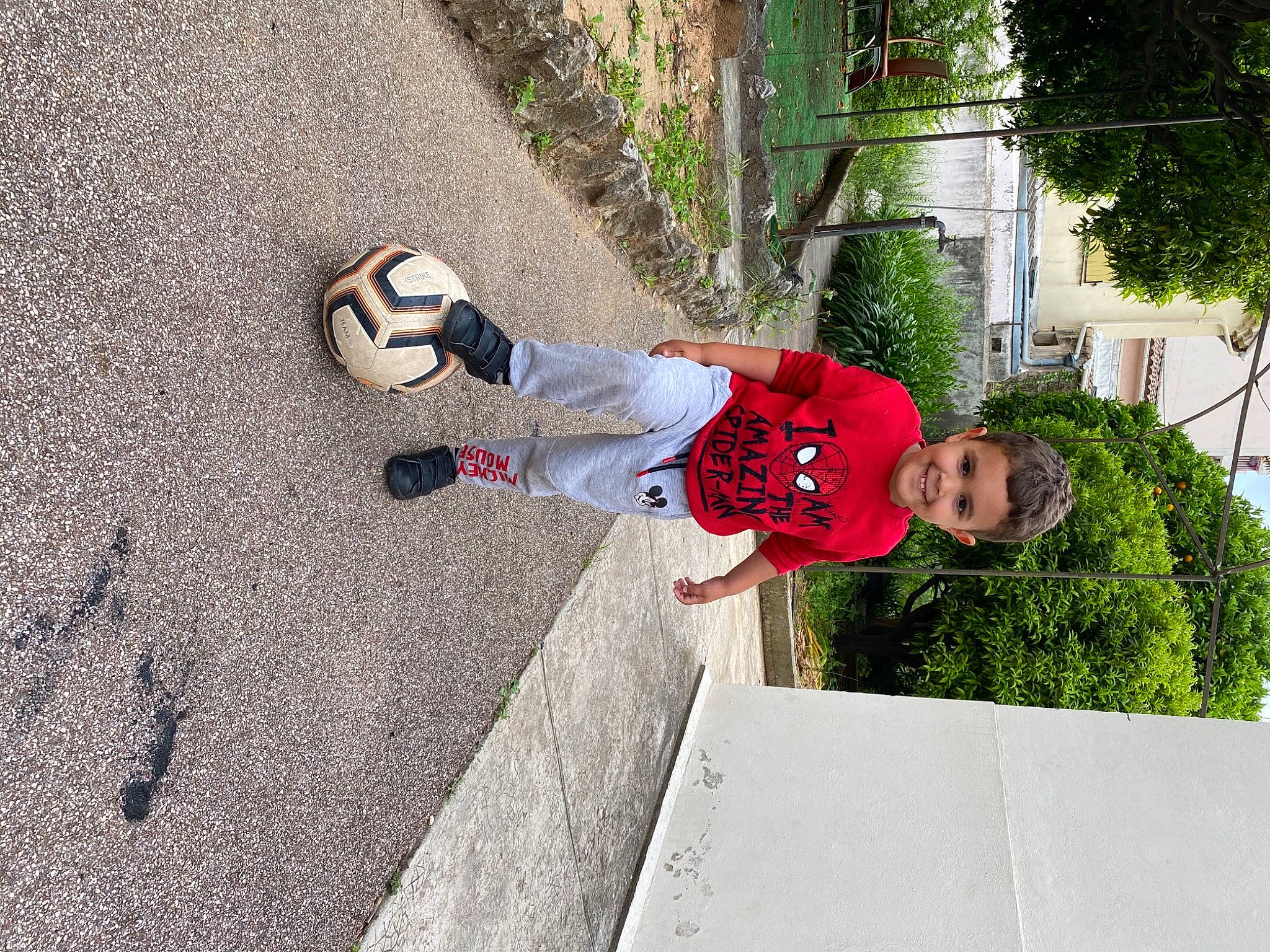 Chahine participe au concours pour gagner de l'argent avec cette photo : asphalt, ball, carmine, concrete, flooring, football, fun, grass, joy, leisure, people_in_nature, person, plant, recreation, sidewalk, soccer, soil, sports_equipment, t_shirt, toddler