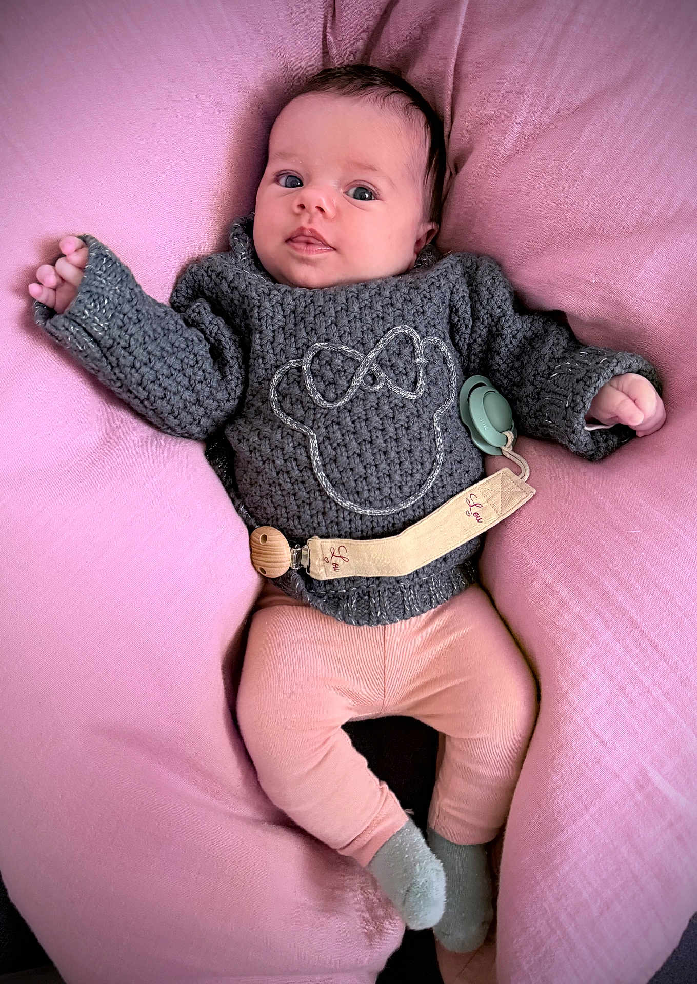 Lou a rejoint le concours — aidez-le/la à gagner de superbes lots ! baby, infant, cushion, pink, gray_sweater, knitwear, leggings, socks, face, person, child, cute, indoor, soft_texture, comfort, resting, portrait, young_child, cozy, pacifier_clip