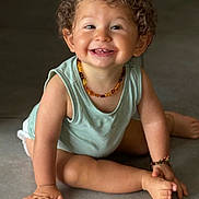 Roméo a rejoint le concours — aidez-le/la à gagner de superbes lots ! baby, child, curly_hair, cute, floor, foot, green_top, hand, happy, indoors, infant, joyful, necklace, person, playful, sitting, skin, smiling, tile, young_child