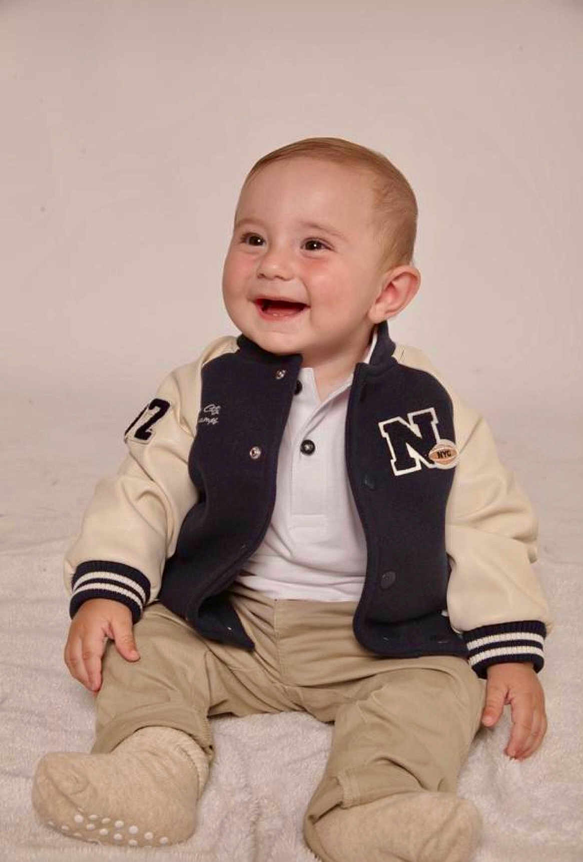 Christopher joined the competition — help win amazing prizes! baby, child, smile, sitting, jacket, pants, footwear, happy, portrait, indoor, cute, young, infant, clothing, person, face, head, warm, soft, blanket