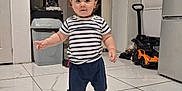 Mathias participe au concours pour gagner de l'argent avec cette photo : toddler, child, indoor, striped_shirt, navy_shorts, shoes, tile_floor, pacifier, toy_car, kitchen, refrigerator, cabinet, trash_can, shadow, person, young_child, cute, standing, home, furniture