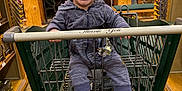 Luka is registered to the contest to win money with this photo: baby, child, shopping_cart, cap, smiling, striped_clothing, footwear, indoor, store, wooden_pillars, shelves, retail, happy, person, infant, flooring, toy, pacifier, casual, shopping