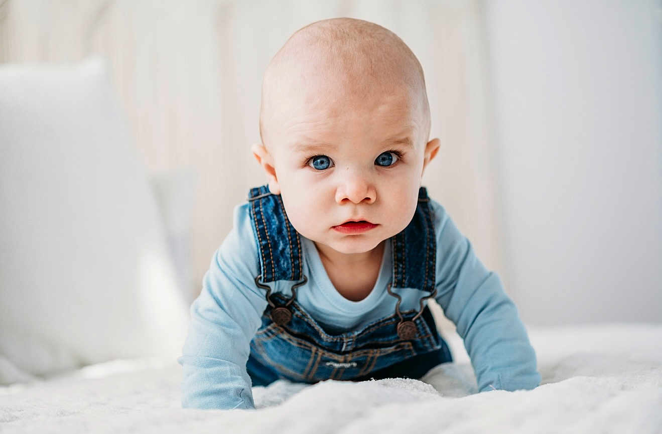 Luka is registered to the contest to win money with this photo: baby, blue_eyes, denim_overalls, crawling, infant, cute, child, indoors, soft_light, white_bed, portrait, serious_expression, clothing, closeup, young_child, head, face, person, baby_boy, looking