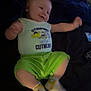 baby, infant, child, smiling, clothing, onesie, socks, green_shorts, bed, blanket, remote_control, happy, cute, lying_down, indoor, person, face, young_child, movement, soft_lighting