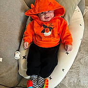 Louka participe au concours pour gagner de l'argent avec cette photo : baby, black_pants, child, clothing, comfort, couch, cozy, cute, face, happy, hoodie, indoor, infant, orange_clothing, person, pillow, playful, smiling, striped_socks, toy
