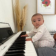 Esmée a rejoint le concours — aidez-le/la à gagner de superbes lots ! art_print, baby, child, curious, expression, furniture, hands, heart_pattern, home, indoor, keyboard, music, pampas_grass, person, piano, plant, portrait, seated, wall, white_clothing