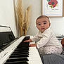 art_print, baby, child, curious, expression, furniture, hands, heart_pattern, home, indoor, keyboard, music, pampas_grass, person, piano, plant, portrait, seated, wall, white_clothing