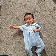 Keeton joined the competition — help win amazing prizes! baby, infant, carpet, blue_outfit, knitwear, smiling, lying_down, white_bow, one_arm_outstretched, cheeky_smile, soft_texture, indoor, child, cute, happy, person, footed_pajamas, short_hair, skin, cozy