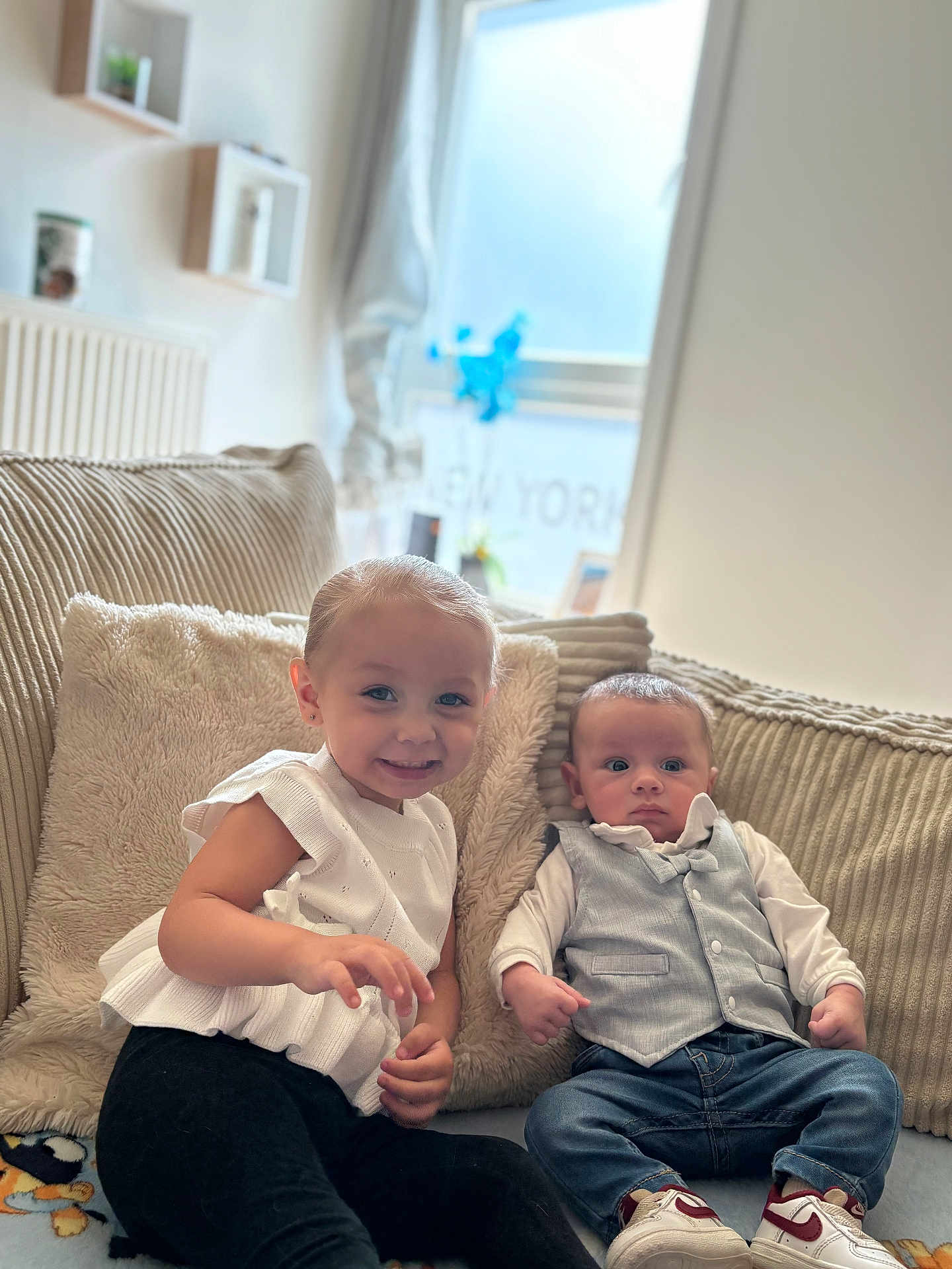 Zelyana participe au concours pour gagner de l'argent avec cette photo : child, toddler, baby, couch, pillow, smiling, curious, white_top, black_pants, vest, jeans, sneakers, indoor, window, natural_light, plush, cozy, furniture, person, portrait