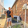 Charlie joined the competition — help win amazing prizes! man, dog, outdoor, brick_wall, air_conditioner, sunny, smiling, shorts, black_shirt, white_shoes, grass, dirt, window, fence, pet, cute, happy, holding, small_dog, daylight