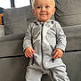 Keylan participe au concours pour gagner de l'argent avec cette photo : toddler, child, smiling, standing, indoors, gray_tracksuit, white_sneakers, couch, door, window, floor, happy, person, casual_clothing, young_child, portrait, home_interior, cute, fashion, feet